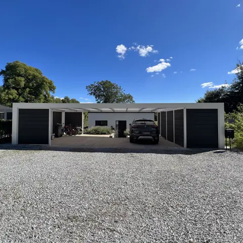 Hvidlakeret funkis carport med skur og plads til cykler og skraldespande