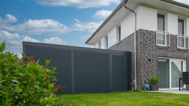 Pulverlakeret antrasitgrå UNA carport med redskabsrum – set fra haven.