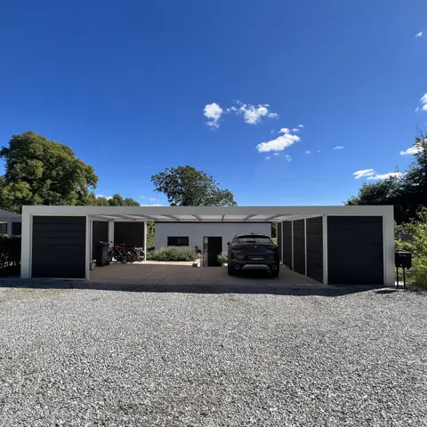 Hvidlakeret funkis carport med skur og plads til cykler og skraldespande